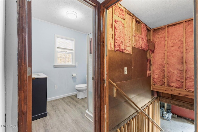 bathroom with a textured ceiling, toilet, wood finished floors, vanity, and baseboards