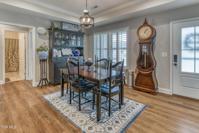 dining room with a raised ceiling, hardwood / wood-style flooring, a chandelier, and ornamental molding