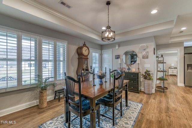 dining room featuring a tray ceiling, ornamental molding, and light hardwood / wood-style flooring