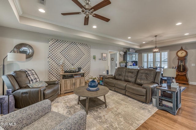 living room featuring light wood-type flooring, ceiling fan with notable chandelier, crown molding, and a raised ceiling