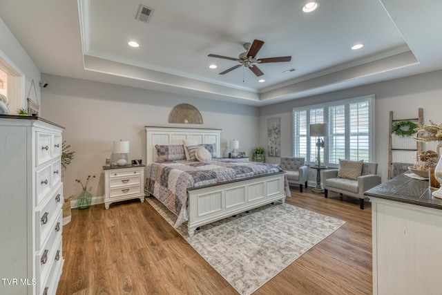 bedroom featuring hardwood / wood-style floors, ceiling fan, a tray ceiling, and crown molding