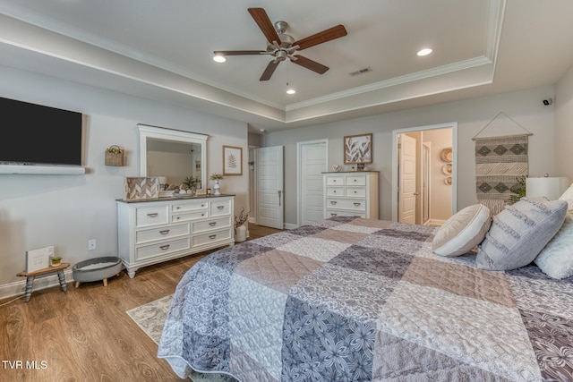 bedroom with ceiling fan, ornamental molding, light wood-type flooring, and a raised ceiling