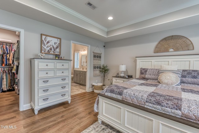 bedroom with a closet, a walk in closet, a tray ceiling, light hardwood / wood-style floors, and crown molding