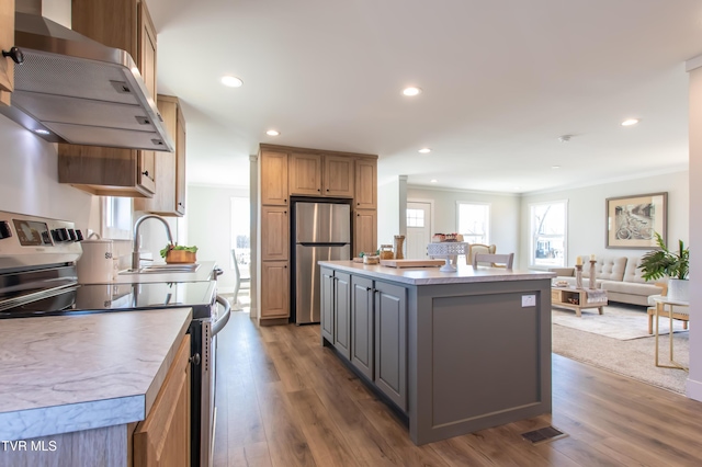 kitchen featuring dark wood-style flooring, stainless steel appliances, open floor plan, a kitchen island, and wall chimney exhaust hood