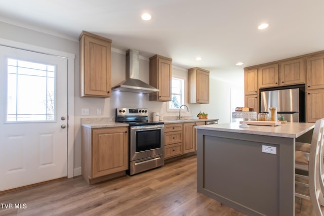 kitchen featuring a center island, stainless steel appliances, light countertops, a sink, and wall chimney range hood