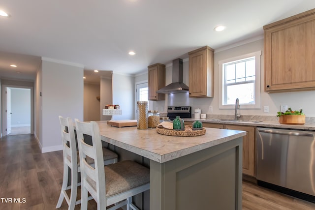 kitchen with light countertops, appliances with stainless steel finishes, a kitchen island, wall chimney range hood, and a sink