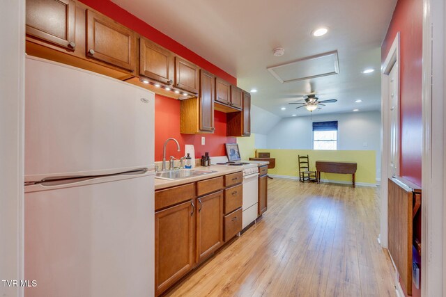 kitchen with a sink, light wood-type flooring, brown cabinets, range, and freestanding refrigerator