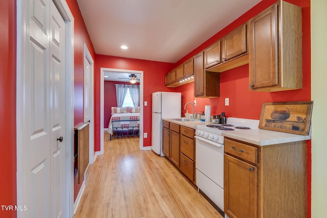 kitchen with white appliances, baseboards, light countertops, light wood-type flooring, and a sink