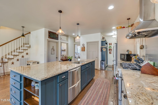 kitchen with island exhaust hood, appliances with stainless steel finishes, a sink, wood finished floors, and blue cabinets