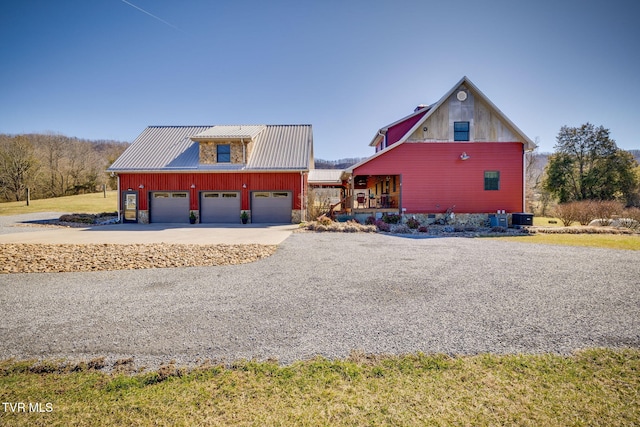 view of front of property with covered porch, an attached garage, central AC unit, metal roof, and driveway