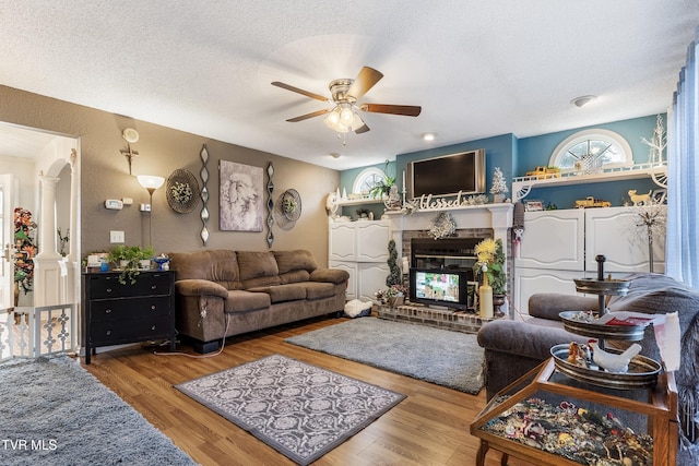 living room with a fireplace, ornate columns, wood-type flooring, and a textured ceiling