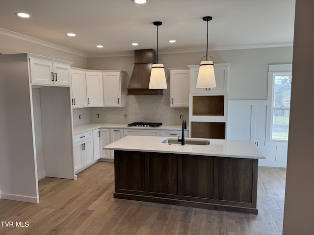 kitchen featuring sink, custom exhaust hood, white cabinetry, and an island with sink