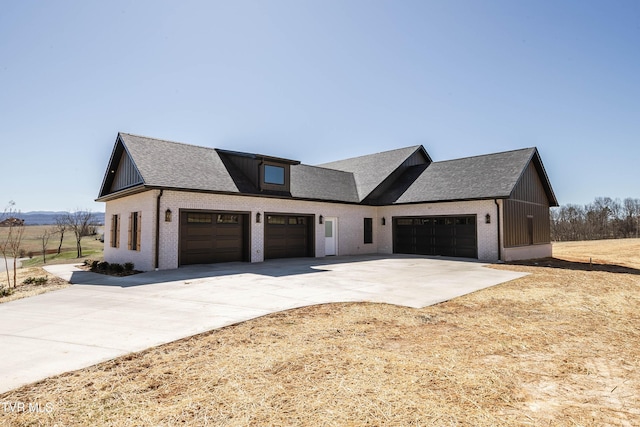 modern farmhouse style home with a shingled roof, brick siding, driveway, and an attached garage