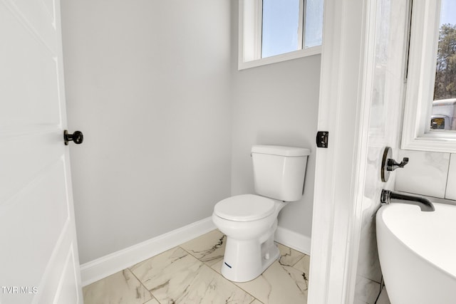 bathroom with marble finish floor, a tub to relax in, toilet, and baseboards