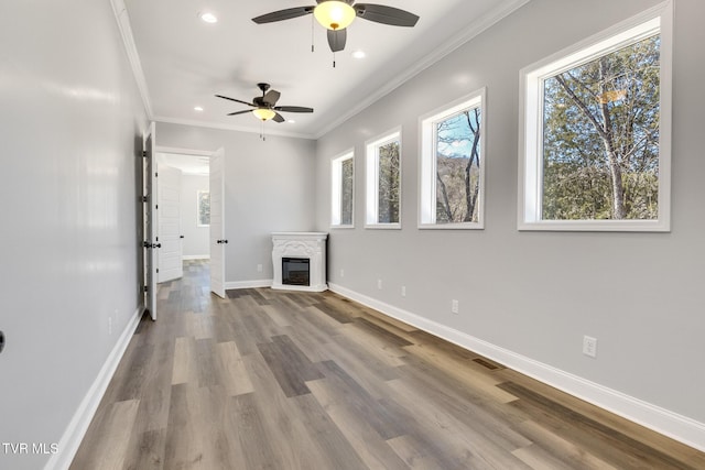 unfurnished living room with recessed lighting, wood finished floors, baseboards, a glass covered fireplace, and crown molding