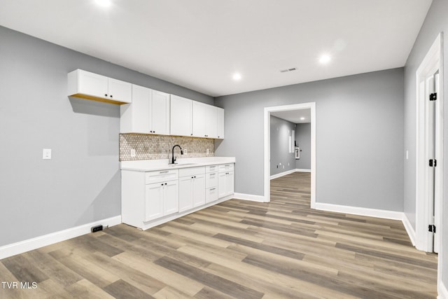 kitchen with light wood-style flooring, a sink, white cabinets, baseboards, and light countertops