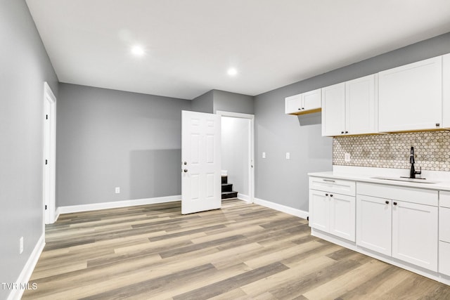 kitchen featuring a sink, white cabinetry, light countertops, decorative backsplash, and light wood finished floors