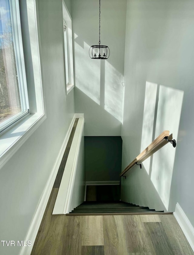 staircase featuring a notable chandelier, baseboards, and wood finished floors