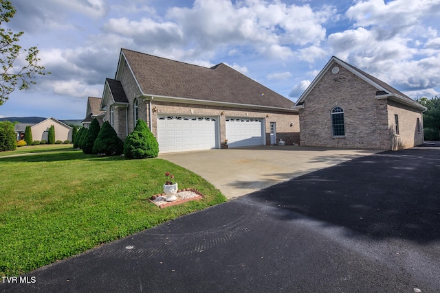 view of side of home with a garage, brick siding, a yard, and driveway