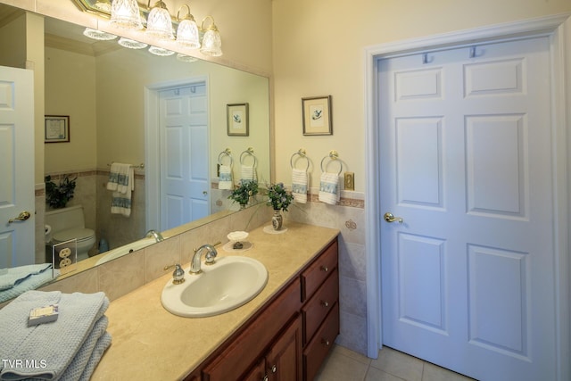 bathroom with toilet, a wainscoted wall, vanity, tile walls, and tile patterned floors