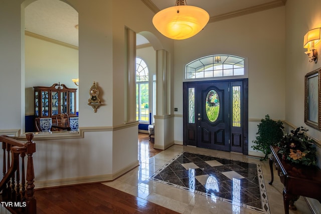 foyer entrance with arched walkways, ornamental molding, a high ceiling, and baseboards