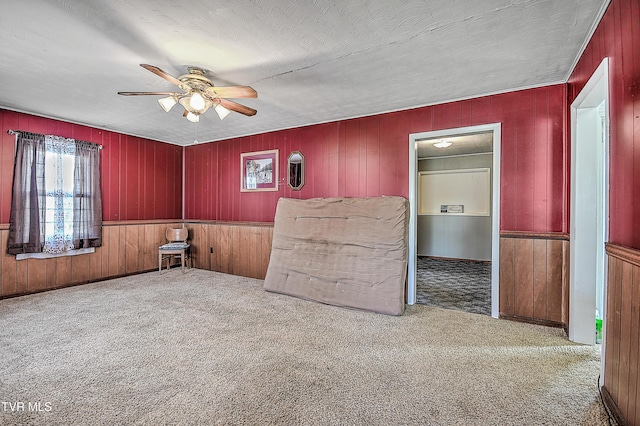 carpeted empty room with a textured ceiling, wooden walls, and ceiling fan