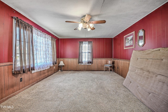 empty room with ceiling fan, carpet flooring, wood walls, and a textured ceiling