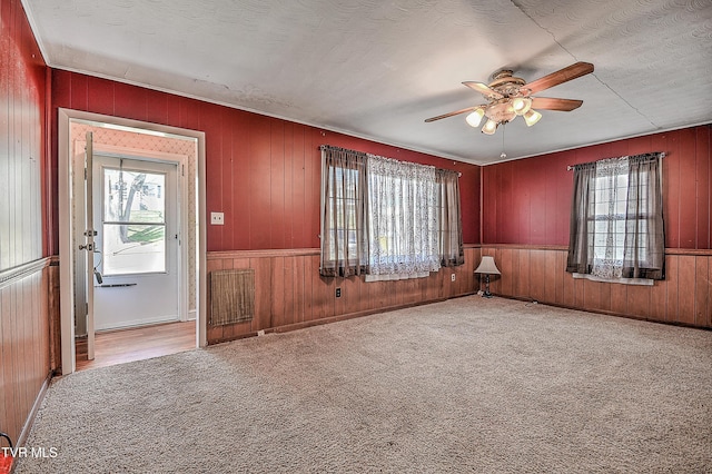 empty room with a textured ceiling, carpet flooring, wood walls, and ceiling fan