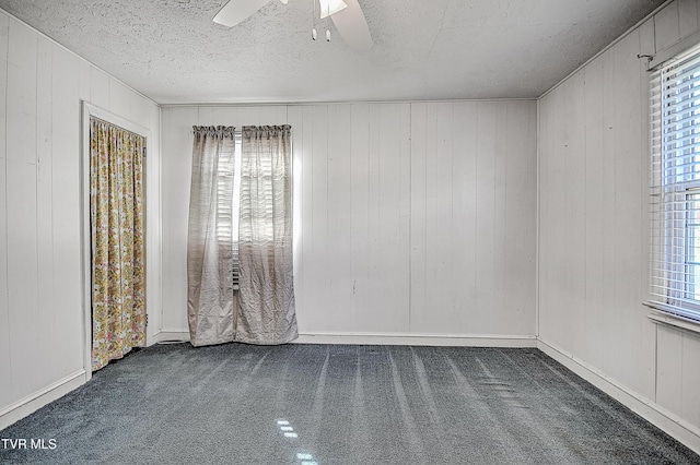 spare room featuring a textured ceiling, dark colored carpet, and ceiling fan