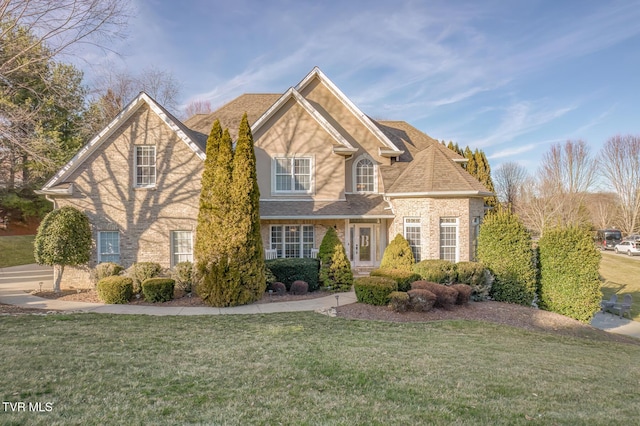 traditional-style home featuring a shingled roof, a front yard, and brick siding