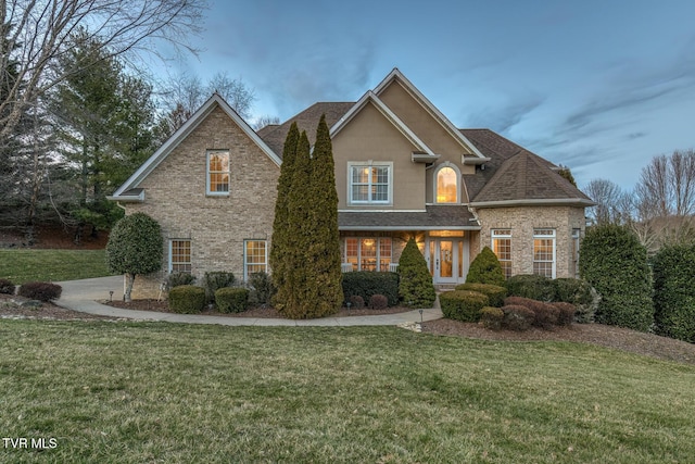 traditional home featuring roof with shingles, a front lawn, and brick siding