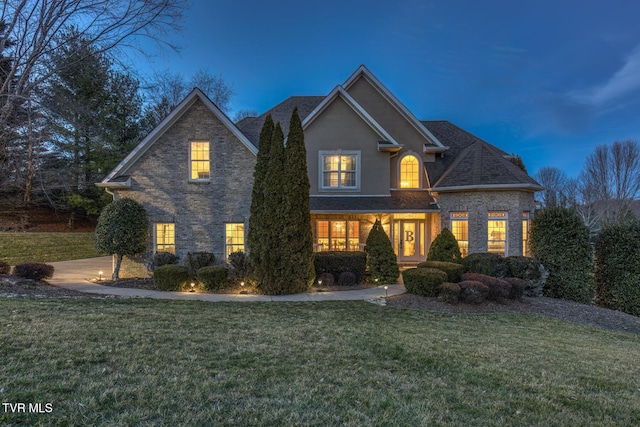 traditional home featuring roof with shingles, a lawn, and stucco siding