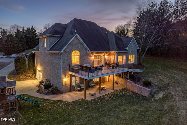 back of property at dusk with a lawn, a playground, and a patio