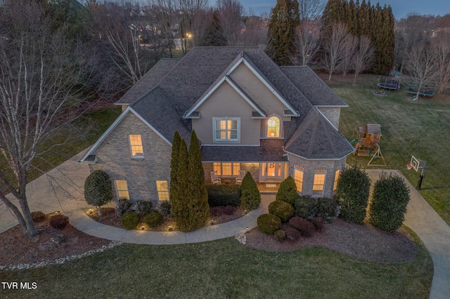 traditional home featuring a trampoline, stucco siding, a shingled roof, stone siding, and a front lawn