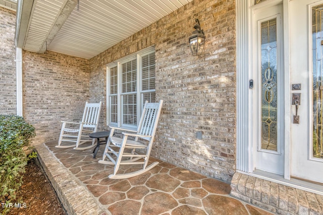 view of exterior entry with a porch and brick siding