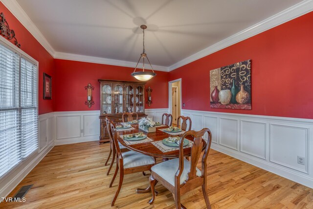 dining space featuring light wood-type flooring, a wainscoted wall, visible vents, and crown molding