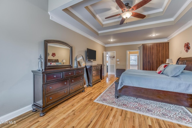 bedroom with ornamental molding, light wood-type flooring, and a raised ceiling