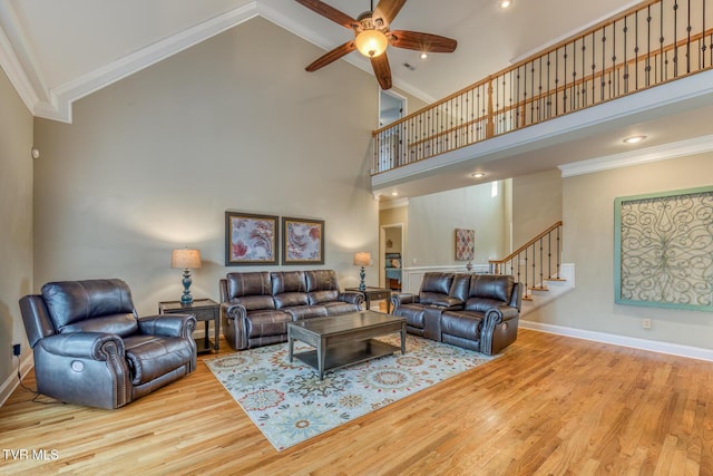 living room with crown molding, light wood-style flooring, high vaulted ceiling, baseboards, and stairs