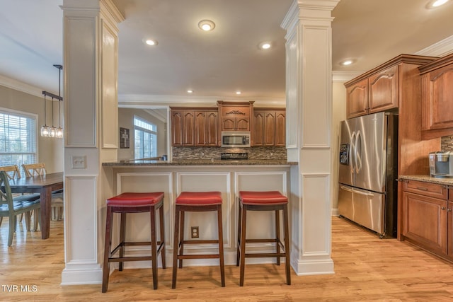 kitchen with brown cabinets, decorative columns, a breakfast bar area, appliances with stainless steel finishes, and dark stone counters