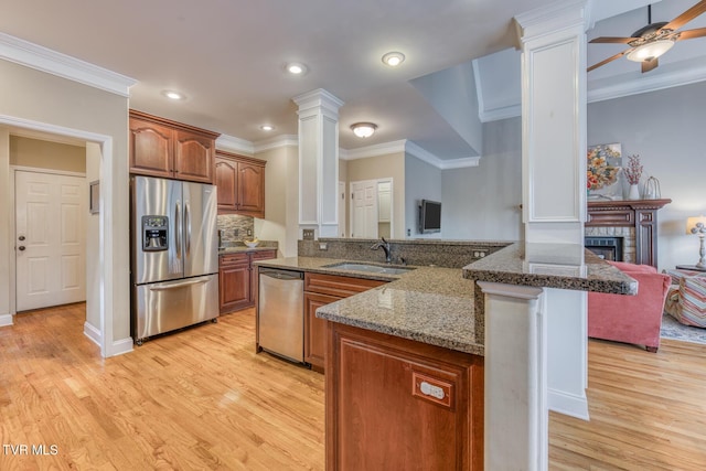 kitchen with brown cabinetry, open floor plan, stainless steel appliances, ornate columns, and a sink