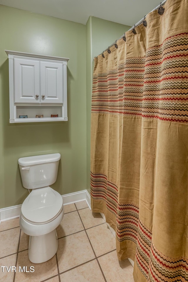 bathroom featuring a shower with shower curtain, toilet, baseboards, and tile patterned floors