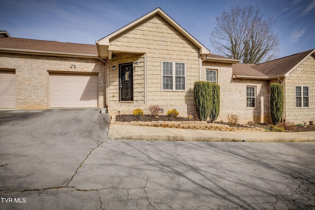 single story home featuring aphalt driveway, brick siding, roof with shingles, an attached garage, and crawl space