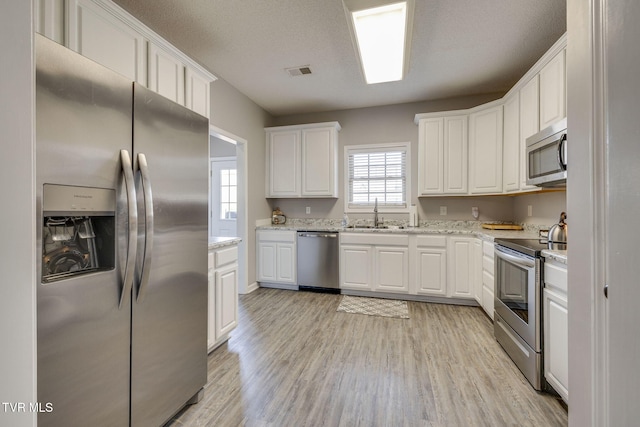 kitchen featuring visible vents, white cabinets, stainless steel appliances, light wood-type flooring, and a sink