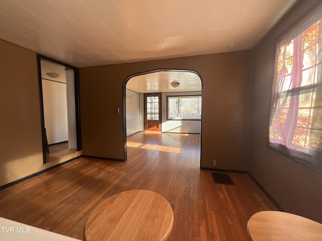 empty room featuring hardwood / wood-style flooring, baseboards, and arched walkways