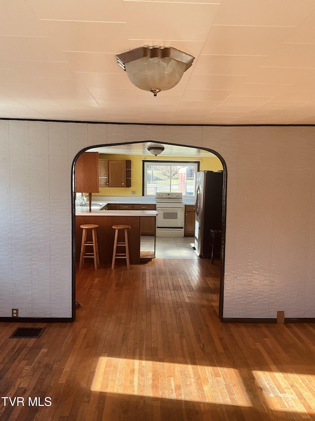 hallway featuring arched walkways, visible vents, and hardwood / wood-style floors