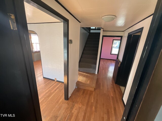 hallway with arched walkways, light wood finished floors, and stairs