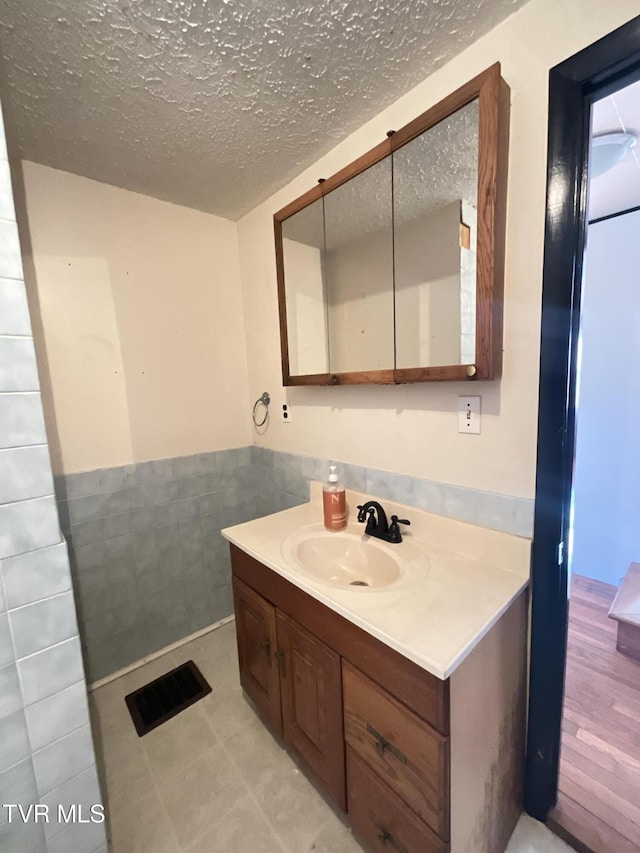 bathroom featuring tile walls, a wainscoted wall, a textured ceiling, and vanity