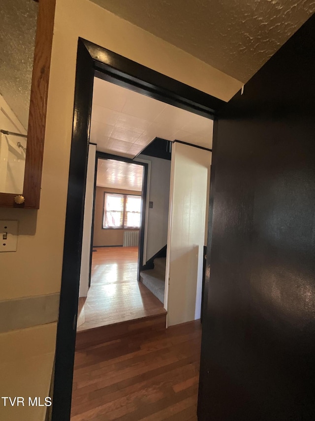 corridor with radiator, stairs, and wood finished floors