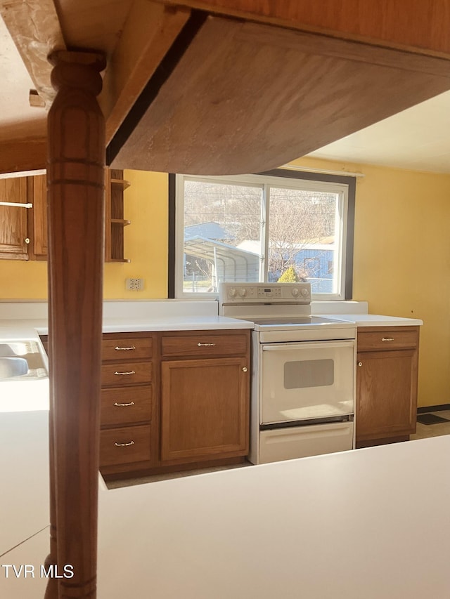 kitchen with light countertops, a wealth of natural light, white range with electric stovetop, and brown cabinets