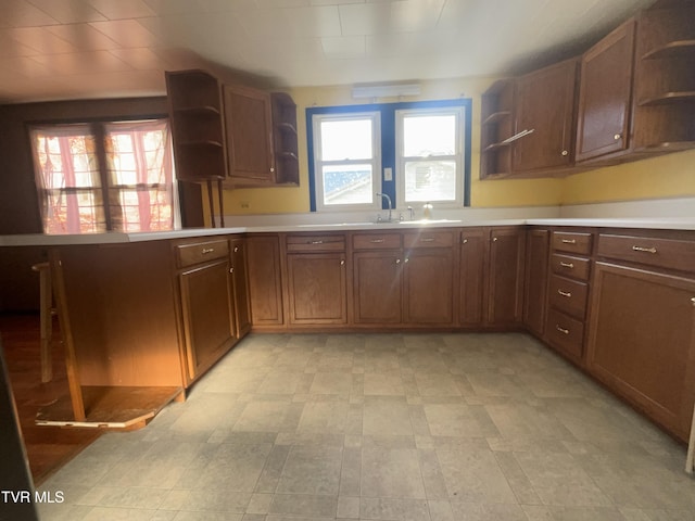 kitchen featuring a peninsula, light countertops, light floors, open shelves, and a sink